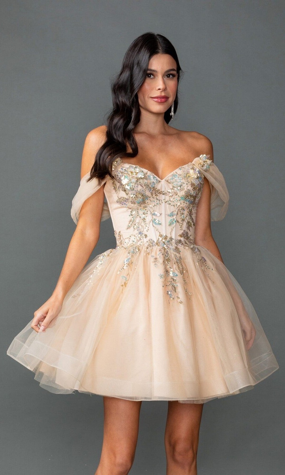 A woman models the Dancing Queen 3423 short prom dress, featuring an off-shoulder beige design with beaded embroidery and a tulle A-line skirt, standing against a plain gray background.